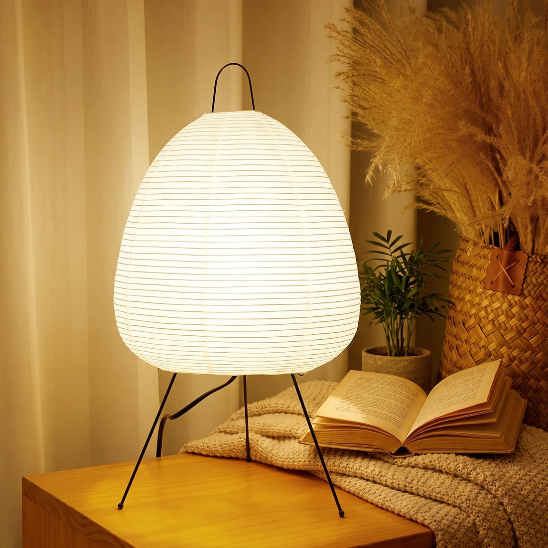 White lamp and vase with dried plants on a wooden nightstand next to a bed.