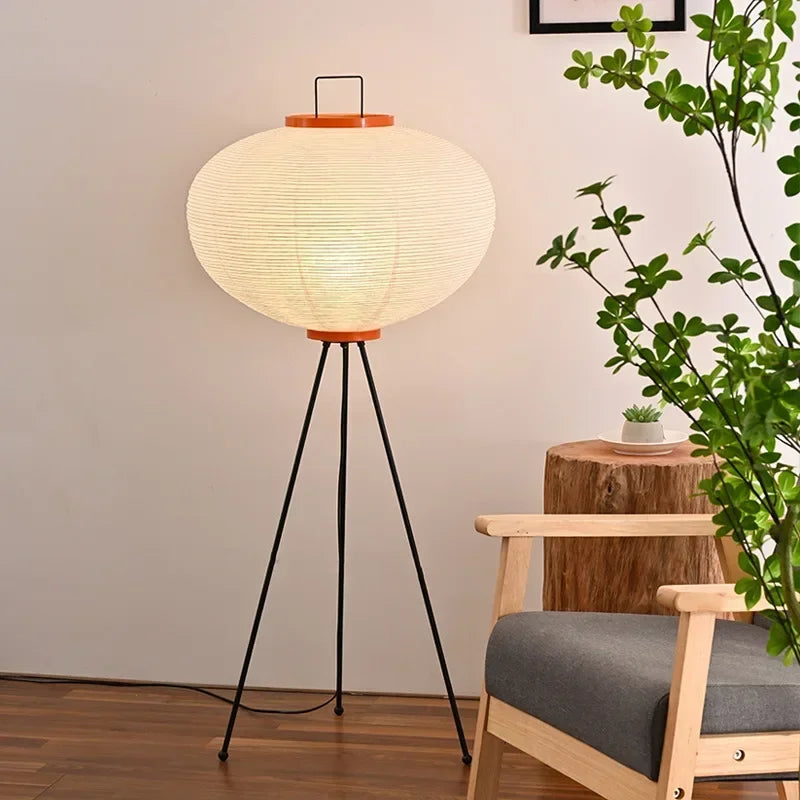 Floor lamp with a round paper shade in a room with a plant and wooden stool.
