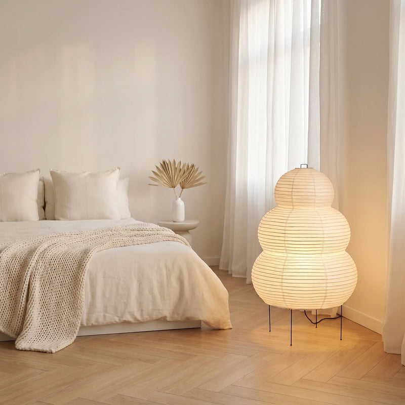 Lummero tiered rice paper floor lamp glowing softly beside a bed – Japandi bedroom evening atmosphere